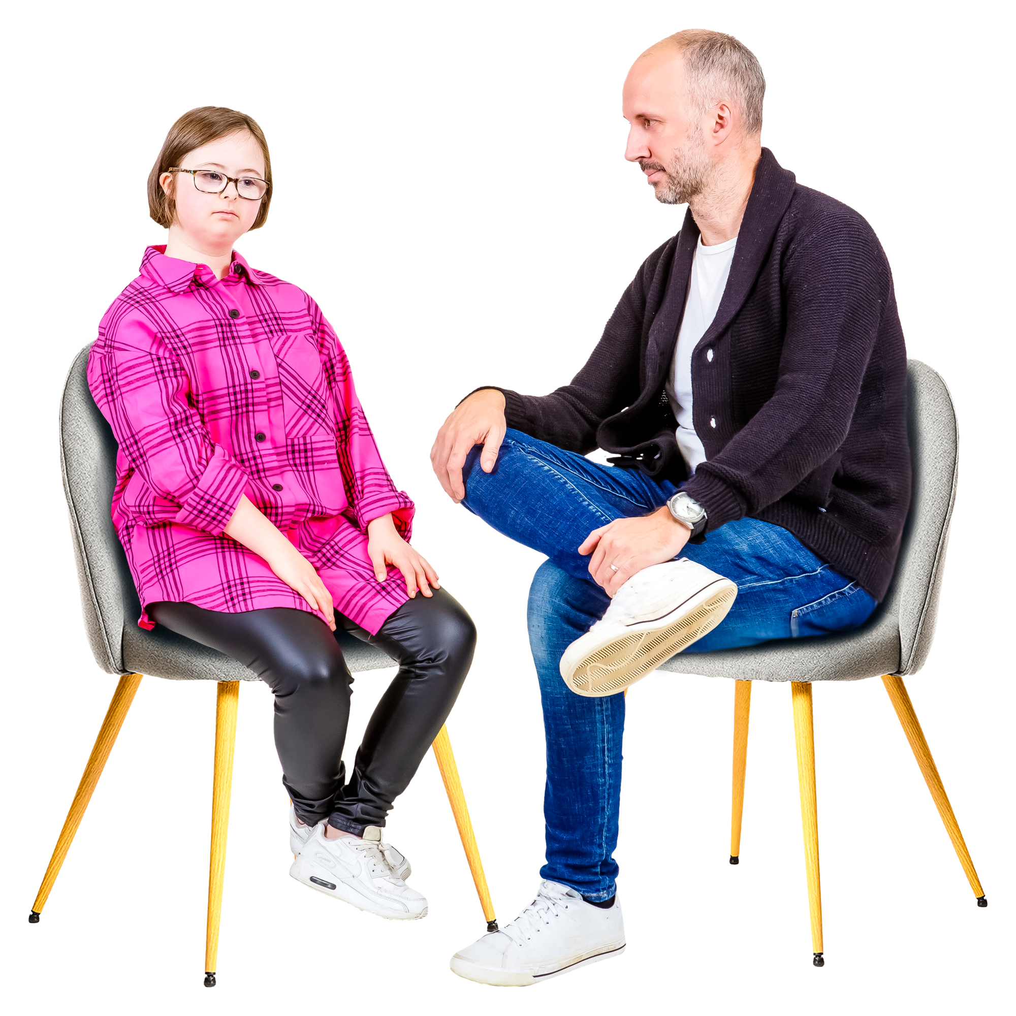 A young girl in a pink plaid shirt and an older man in a black cardigan sitting on chairs, engaged in conversation.