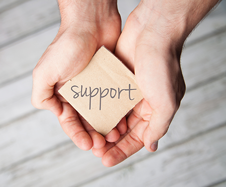 Two handfs holding a square block of wood with support written across the surface