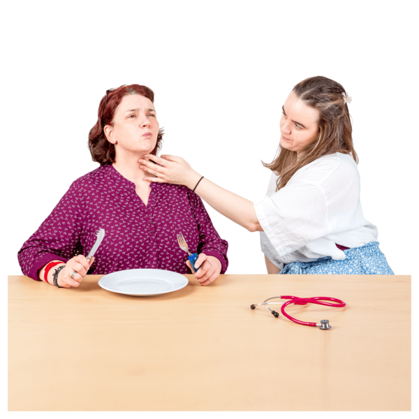 Two people sitting at a table, with one person holding their fingertips to the throat of the other person