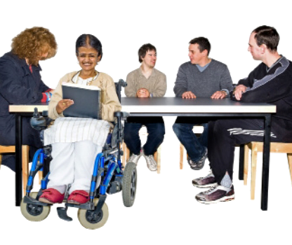 A woman in a wheelchair is holding a document and reading. Behind her is a table with people around it and talking.