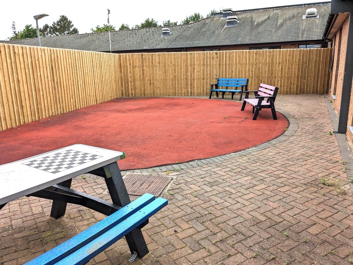 A paved and fenced courtyard with a bench and garden chairs