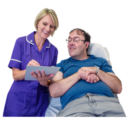 A nurse standing next to a patient lying on his bed. She is holding a document and discussing it with the patient.