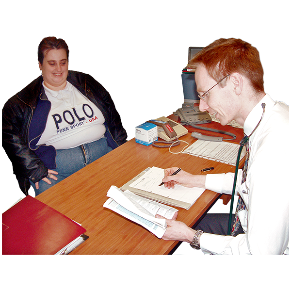 A person sitting in front of a desk. At the other side is a person writing on a piece of paper.
