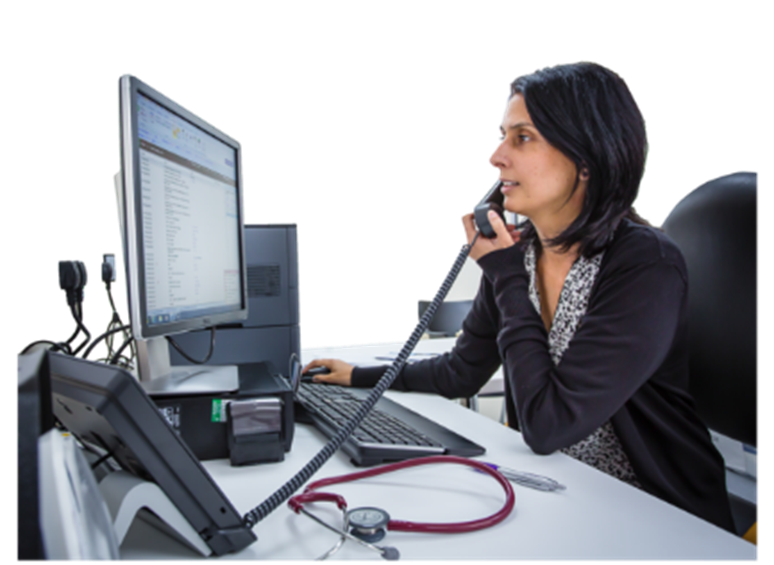A doctor sitting at her desk on the telephone while looking at her computer screen