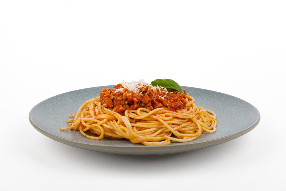 grey plate with serving of spaghetti bolognaise with sprinkle of cheese and basil leaves on top