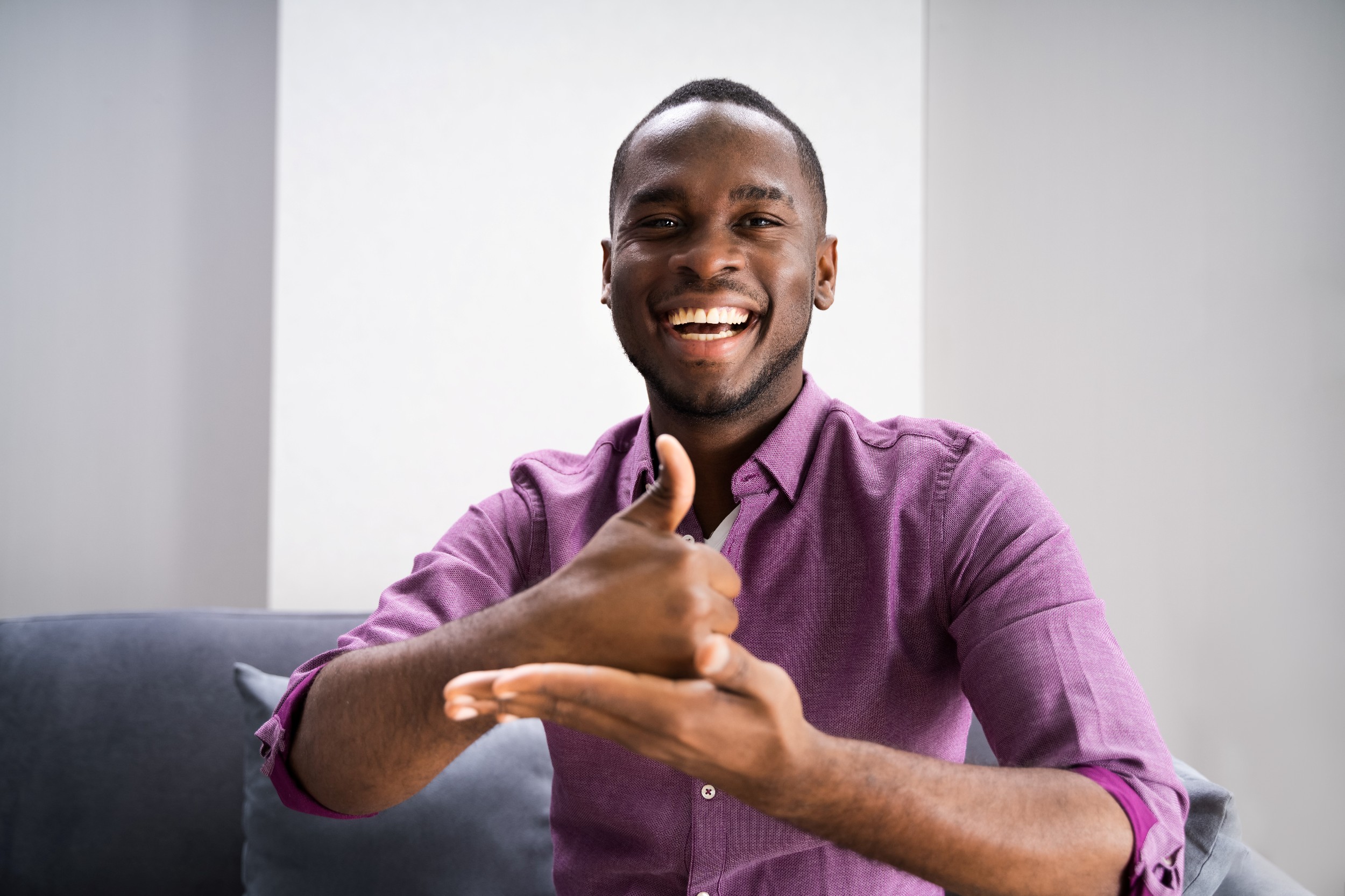 A persin in a purple shirt similing and signing we are happy to help you