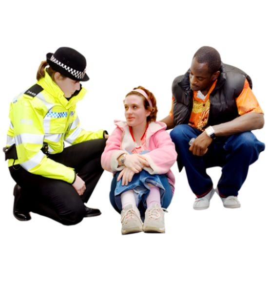 A person is sitting on the ground. There is a carer on the right and a police officer on the left talking.