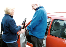 A woman helping a man get in to a car