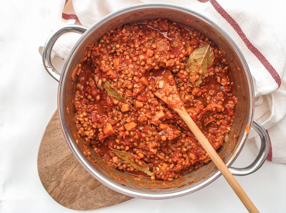 Pan on wooden board with lentil ragu cooking and wooden spoon in the pan