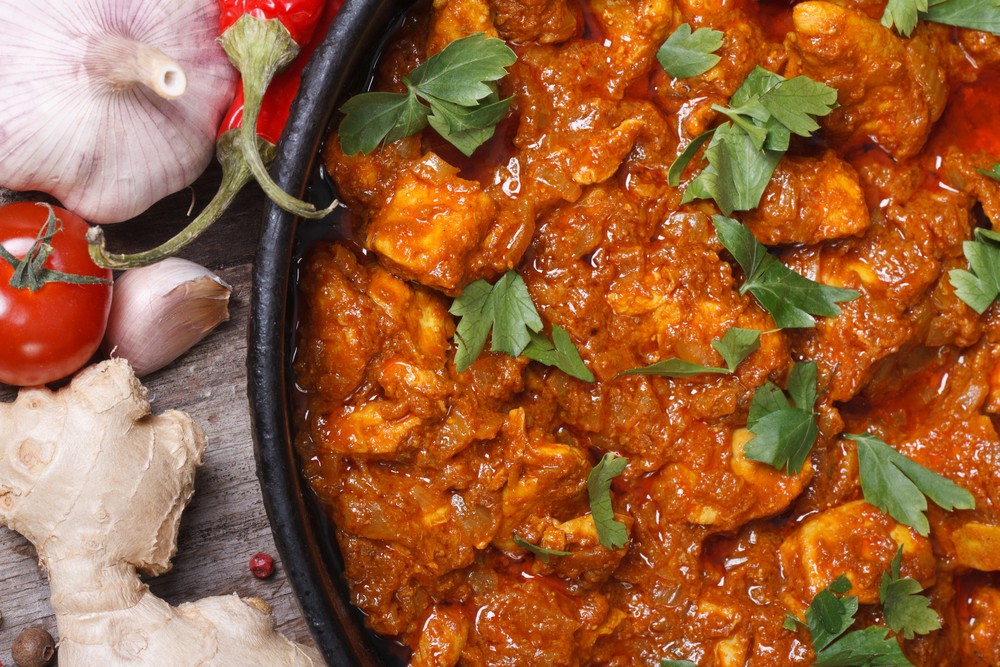 Close up of chicken curry cooking next to ingredients of tomatoes and ginger