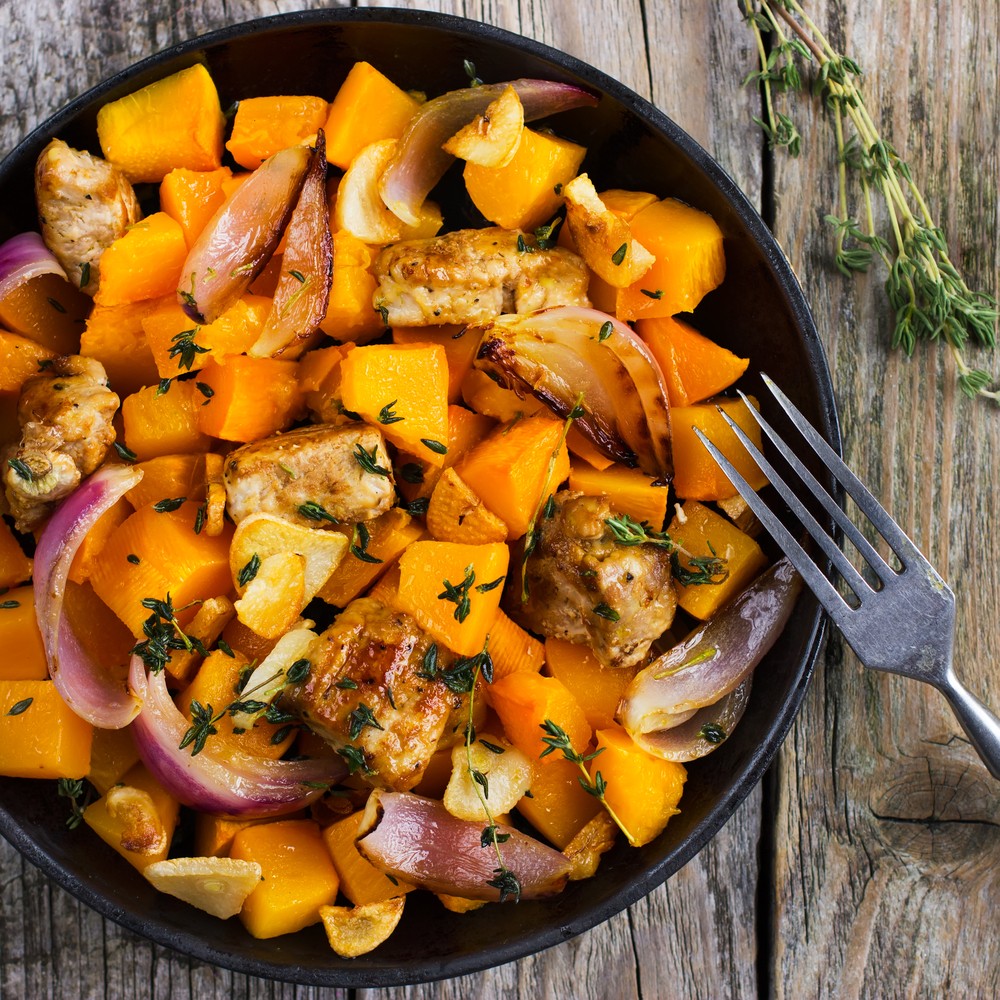 Black plate containing harissa chicken portions and butternut squash pieces with sprig of rosemary and a fork on the table