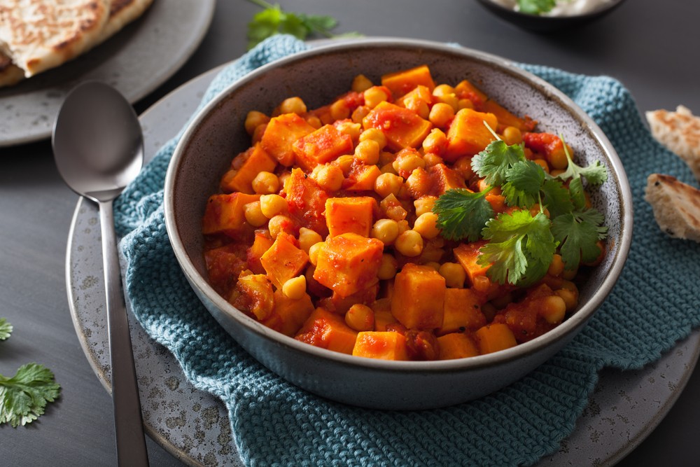 bowl of sweet potato and chickpea curry on blue napkin and grey platter and table, with spoon