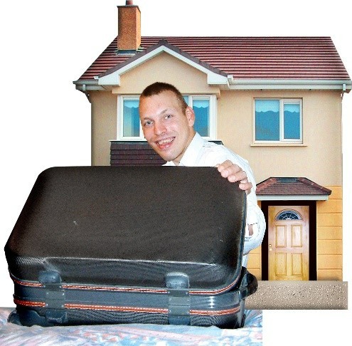 A man carrying a suit case in front of a house