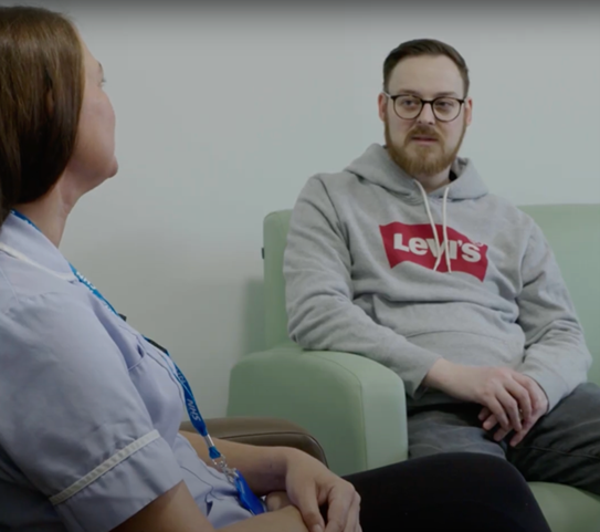 A patient sitting on a couch talking to a nurse