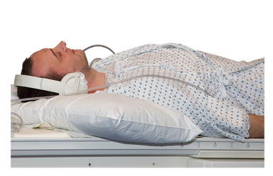 A man in a hospital gown lying on a hospital bed wearing earphones