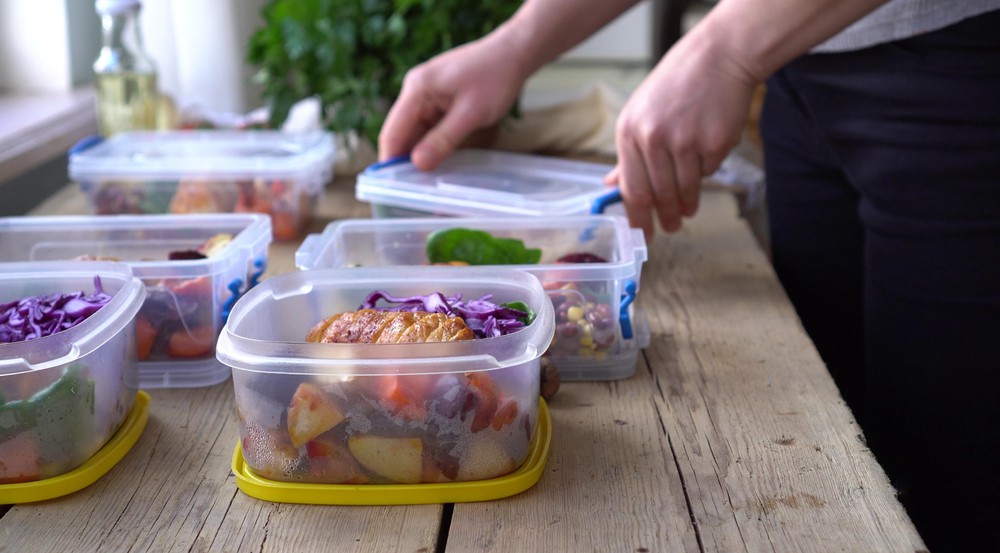 hands of a person portioning leftover food into separate tubs for freezing